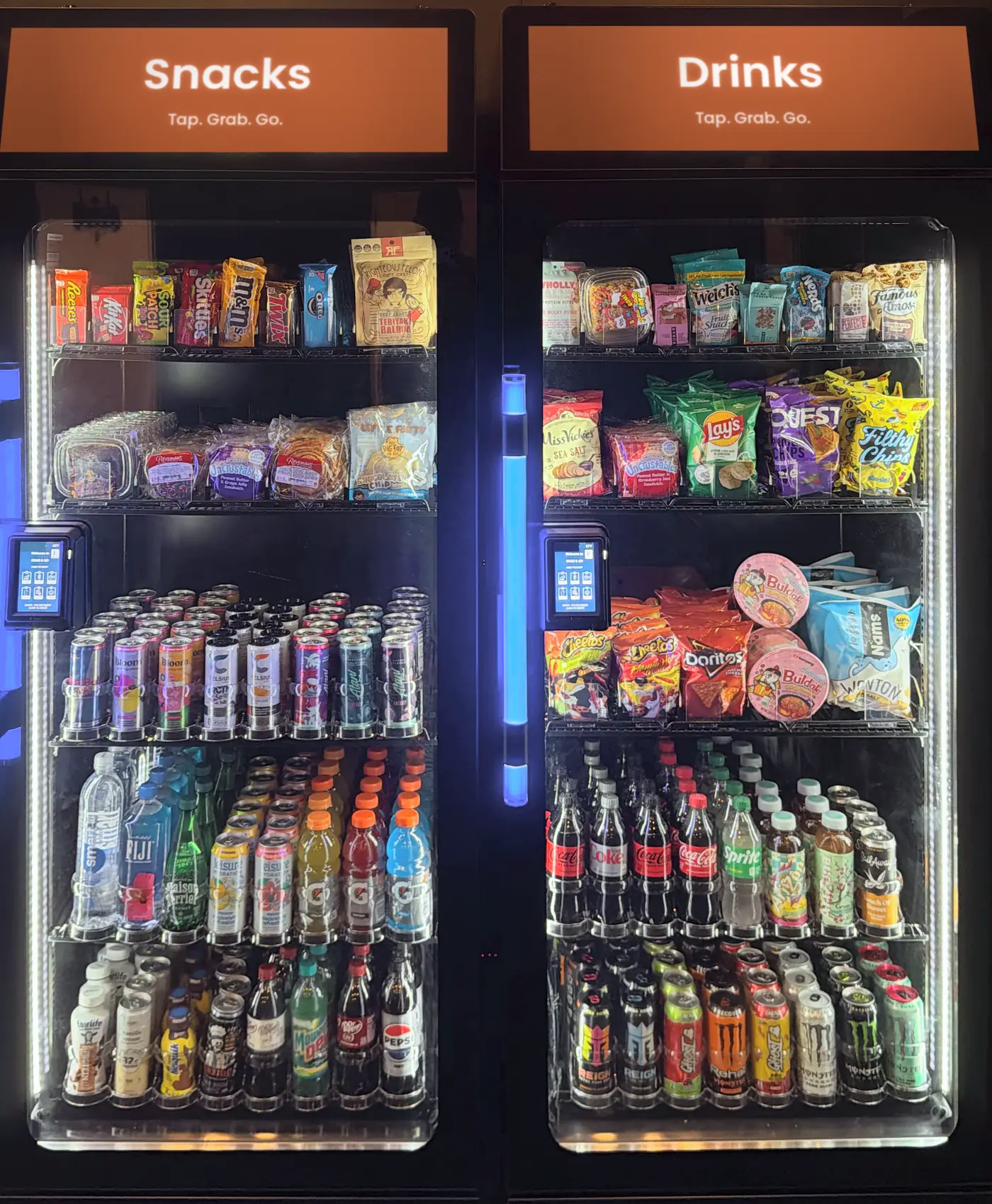 Two Brown Bear smart coolers, lit and stocked with snacks and cold drinks, with Snacks and Drinks screens on top and a tap-to-pay reader on each door.