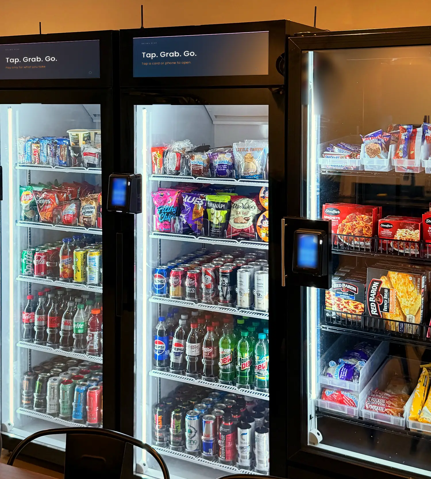 Brown Bear glass-door smart coolers in a break room, lit and fully stocked, each with a tap-to-pay reader on the door.