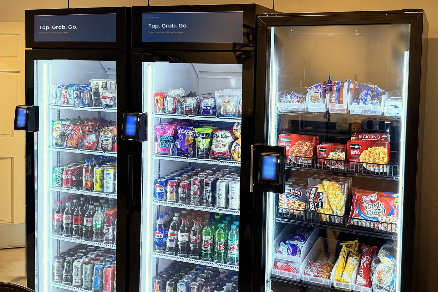 Three Brown Bear smart coolers, lit and stocked, beside the table in a break room.