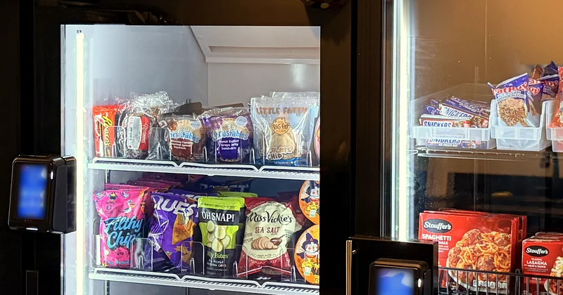 Stocked smart cooler shelves with a tap-to-pay reader on the door.