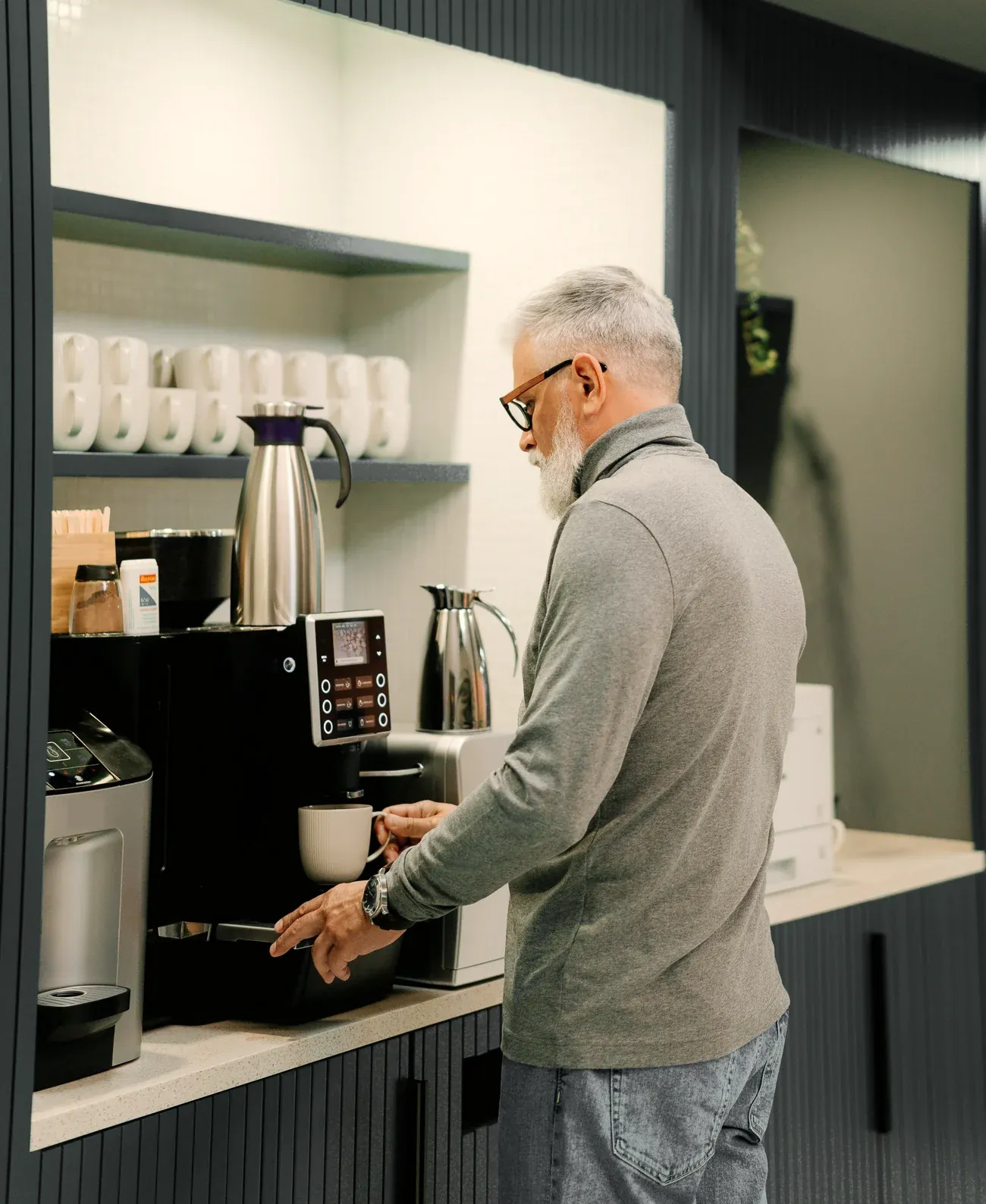 A man pouring a fresh cup from a bean-to-cup coffee machine in an office break room.