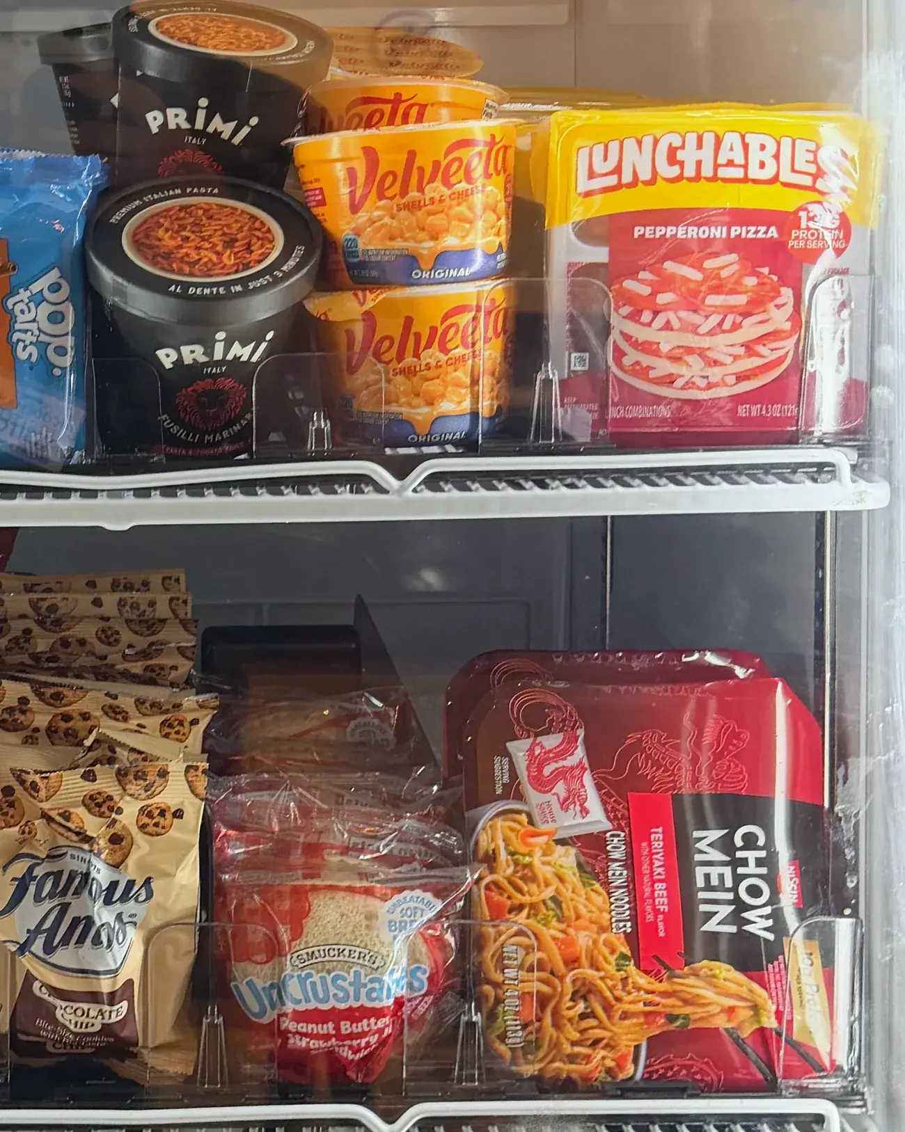 Smart cooler shelves stocked with pasta bowls, mac and cheese cups, Lunchables, chow mein and snacks.