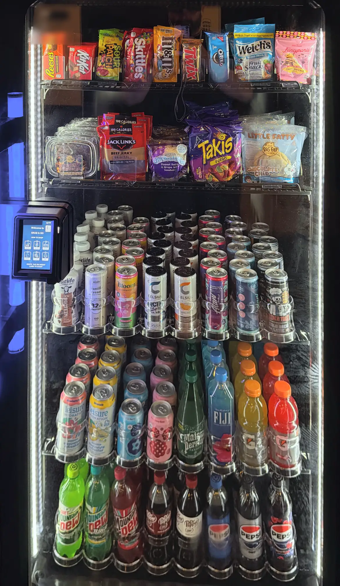 A Brown Bear smart cooler, lit and stocked with snacks, energy drinks and sodas, with a tap-to-pay reader on the door.