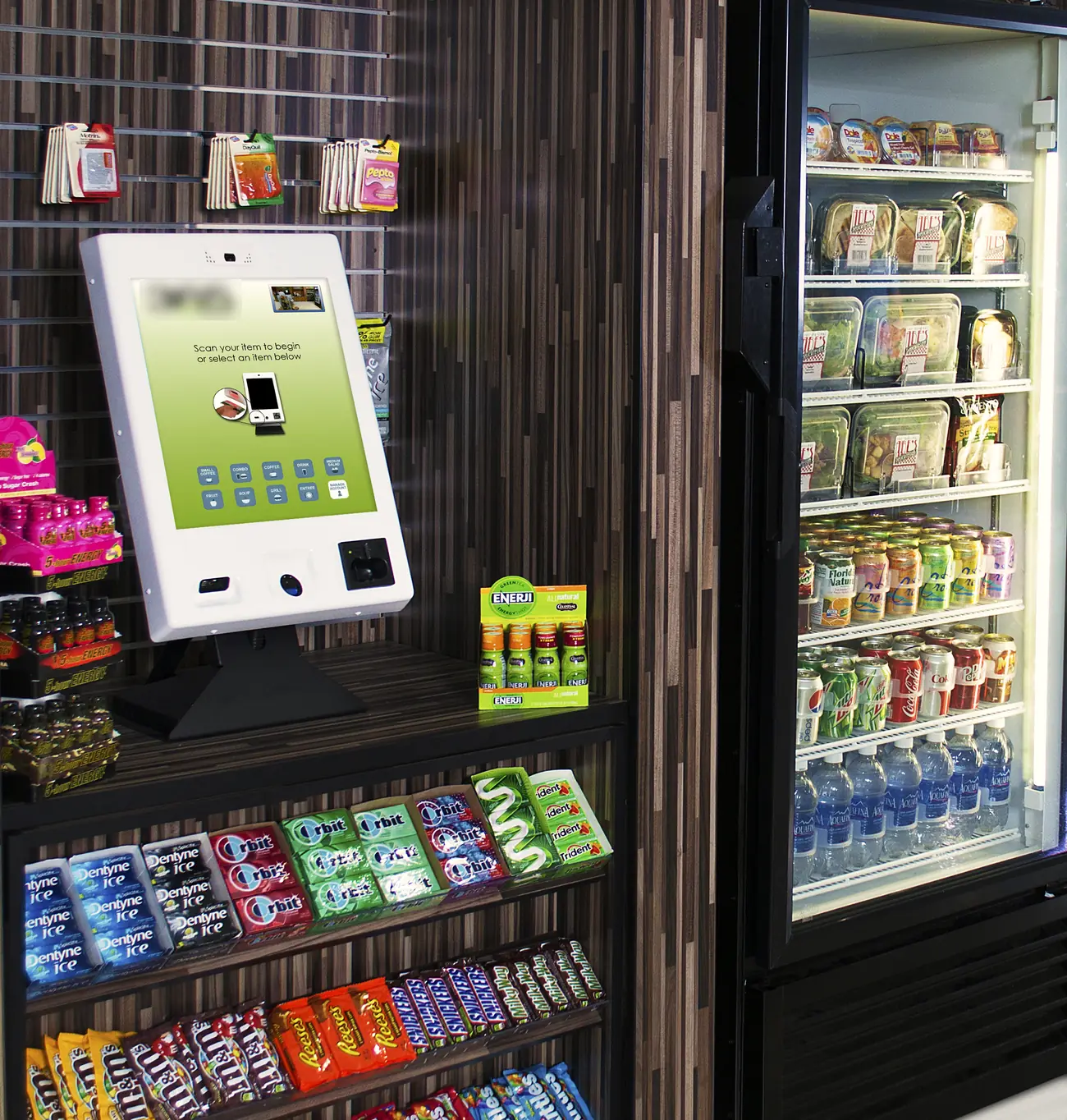 A micro-market with a pay kiosk, snack shelves and glass-door coolers of fresh food and drinks.